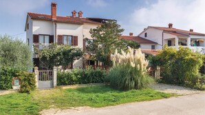 Una casa de dues plantes amb un balcó, envoltada de vegetació i un cel serè.