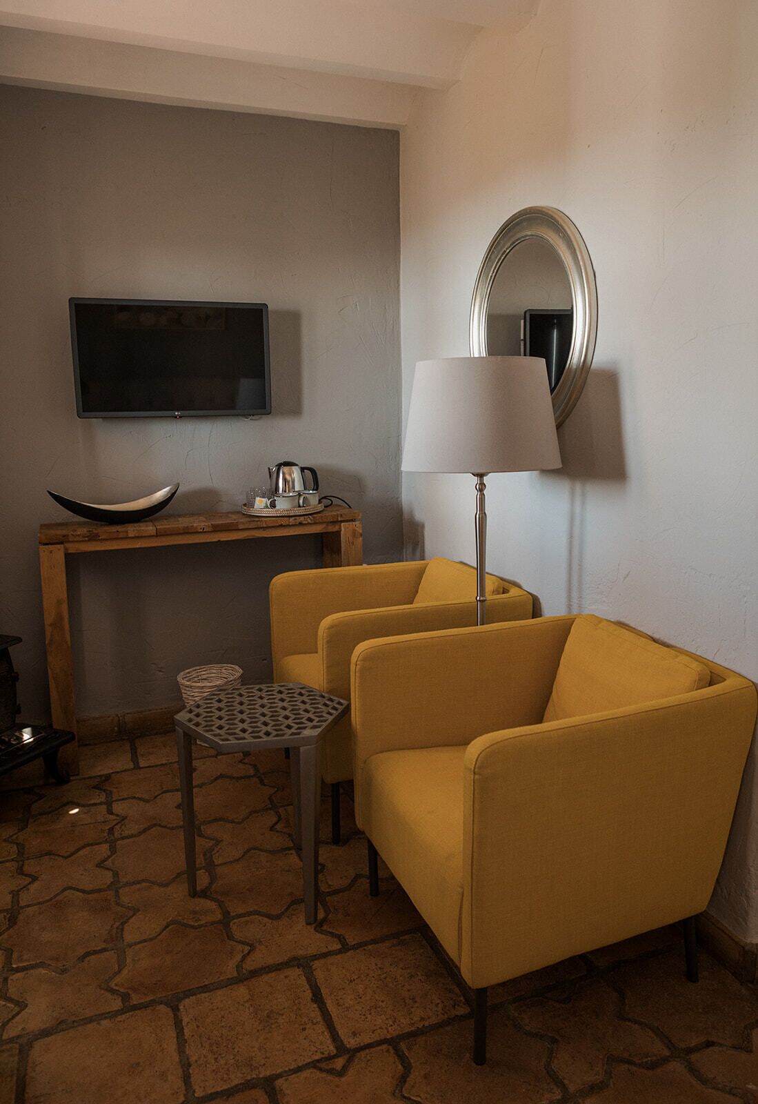 Una habitación con un escritorio de madera, un televisor, un sillón amarillo, una mesita pequeña y una lámpara de pie.