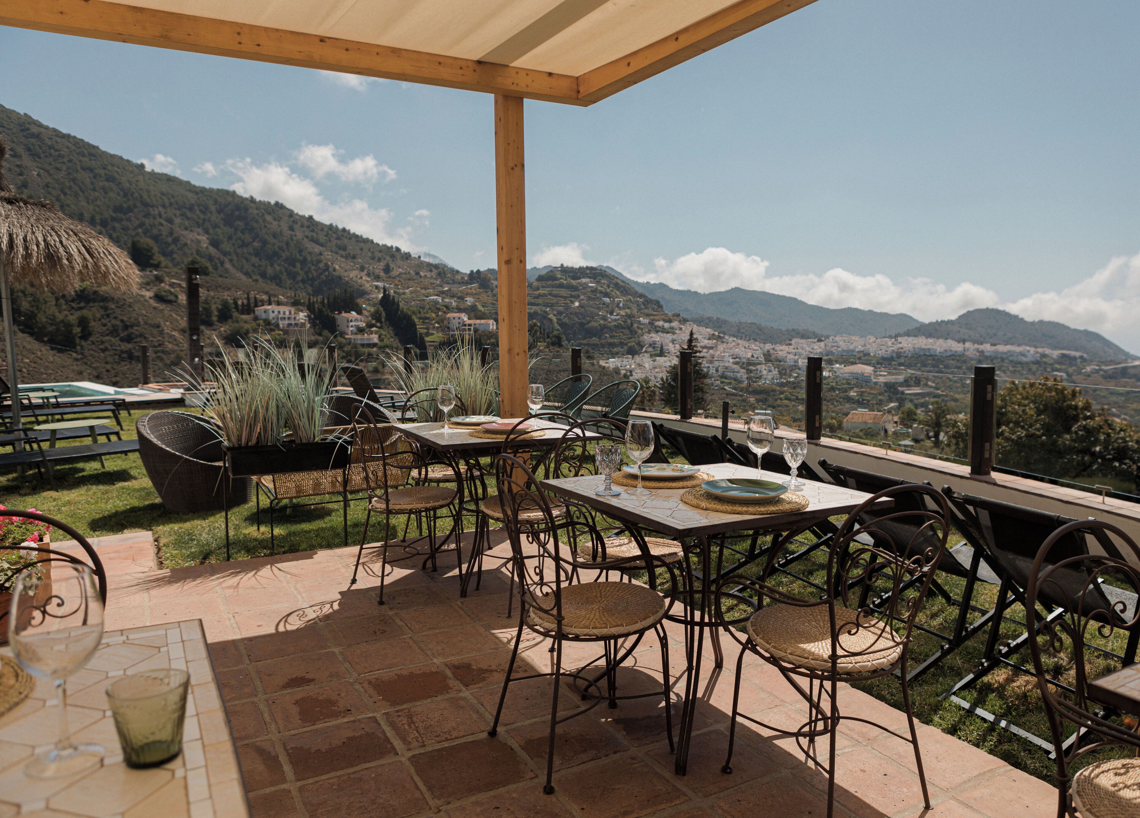 An outdoor patio with tables and chairs, overlooking a scenic view of a town and mountains.