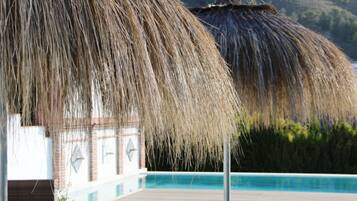 Un espace aménagé au bord de la piscine, doté de parasols en chaume et offrant une vue dégagée sur la piscine.