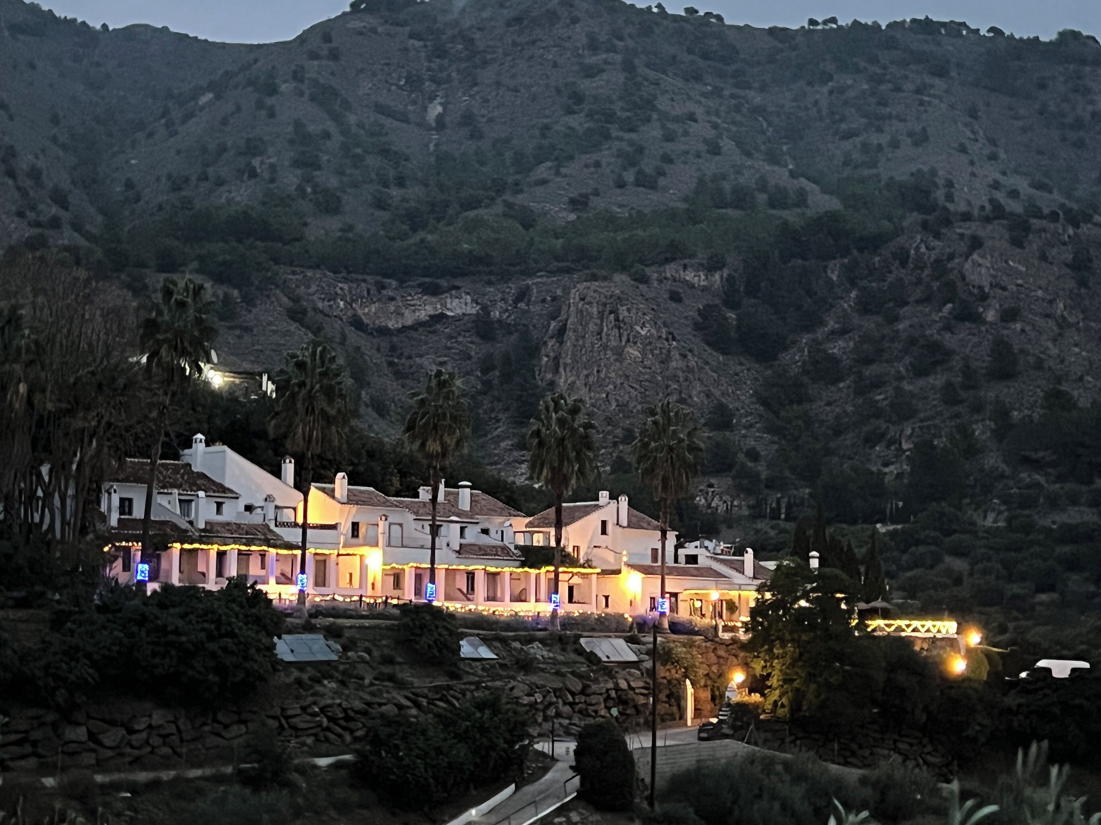 A hillside hotel with multiple buildings, stone walls, and palm trees.