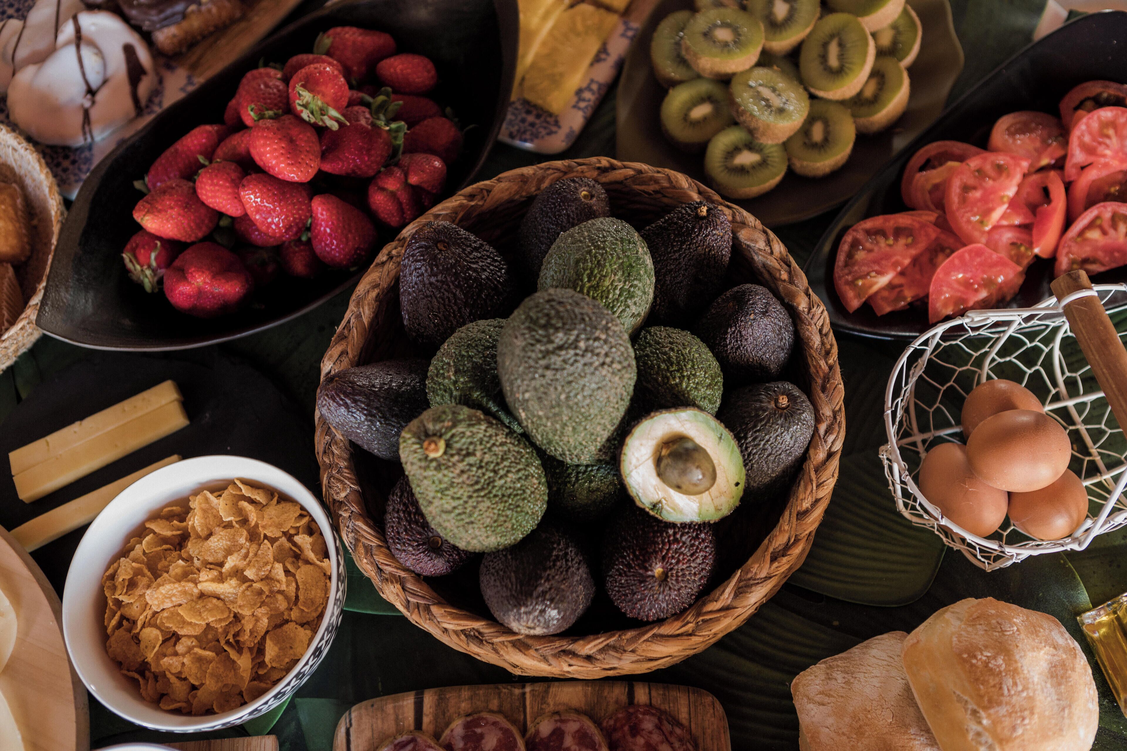 A variety of fruits and vegetables, including avocados, strawberries, and kiwi slices, arranged on a table.