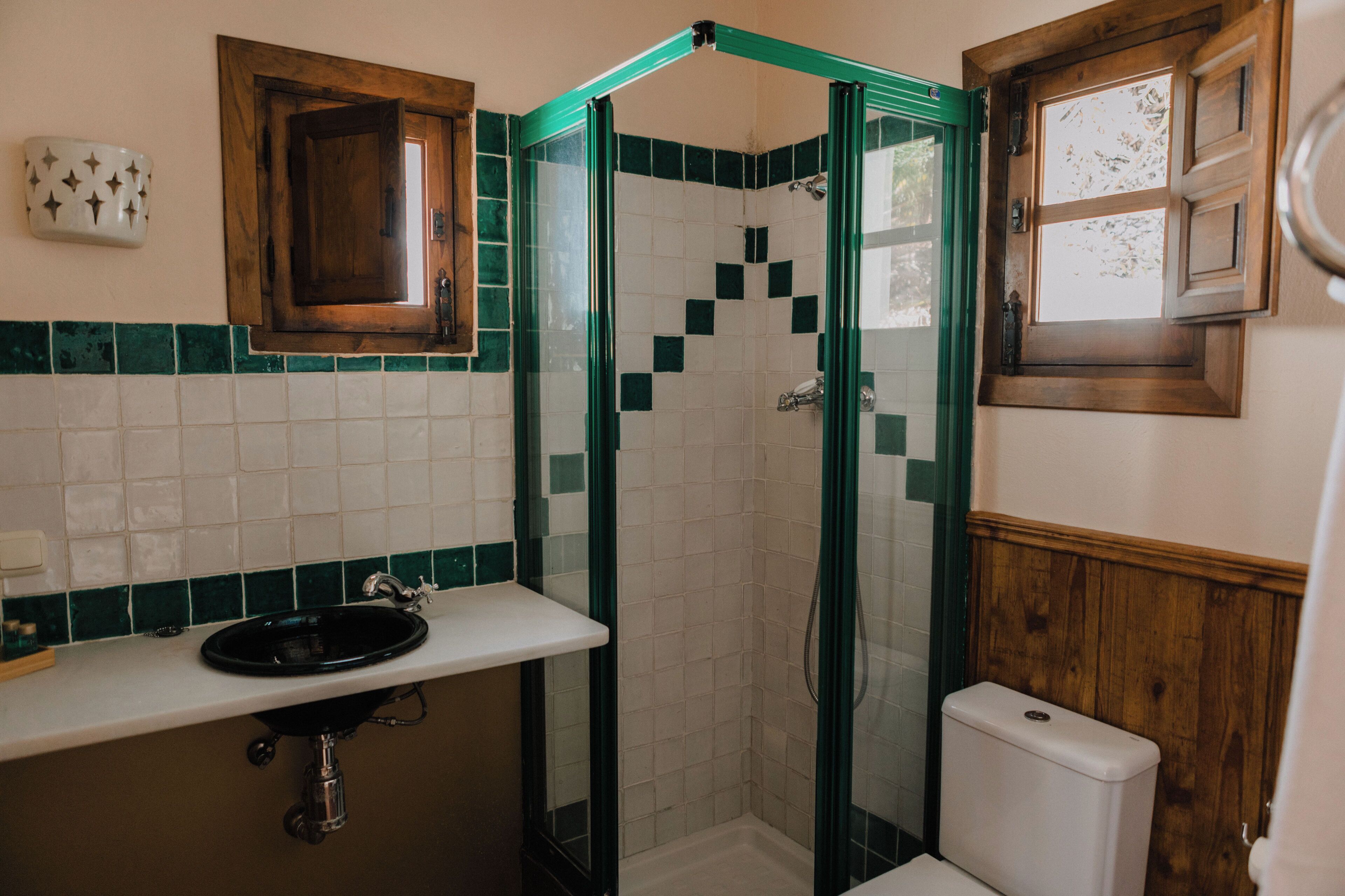 Un baño con un lavabo blanco, un mueble de madera, una ducha con azulejos verdes y un inodoro.