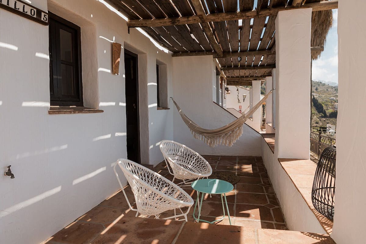 Un espacio exterior cubierto con dos sillas de mimbre blanco, una hamaca y vistas del paisaje.