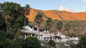 A coastal villa with multiple white buildings, palm trees, and a hillside with autumn-colored trees. - La Posada Morisca (Frigiliana)