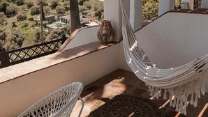 A hammock chair and a wicker chair on a terrace with a view of a hilly landscape. - La Posada Morisca (Frigiliana)