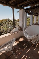 Una silla hamaca y una silla de mimbre en una terraza con vistas a un paisaje montañoso.