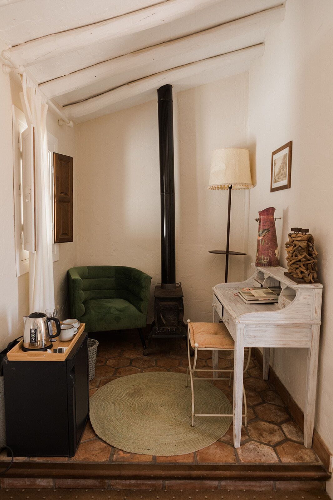 Een gezellige kamer met een groene stoel, een klein tafeltje met een lamp, een open haard en een rustieke inrichting.