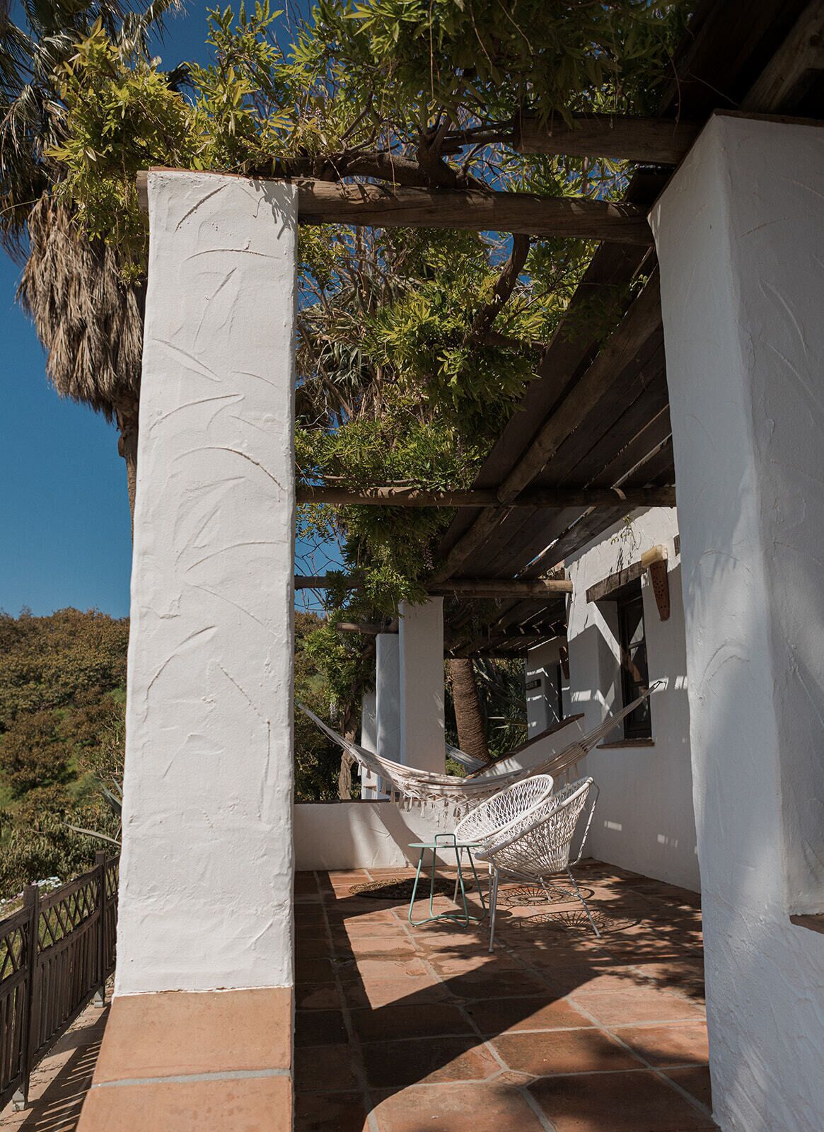 En hvid bygning med hængekøje og hvid stol under et træpergola.