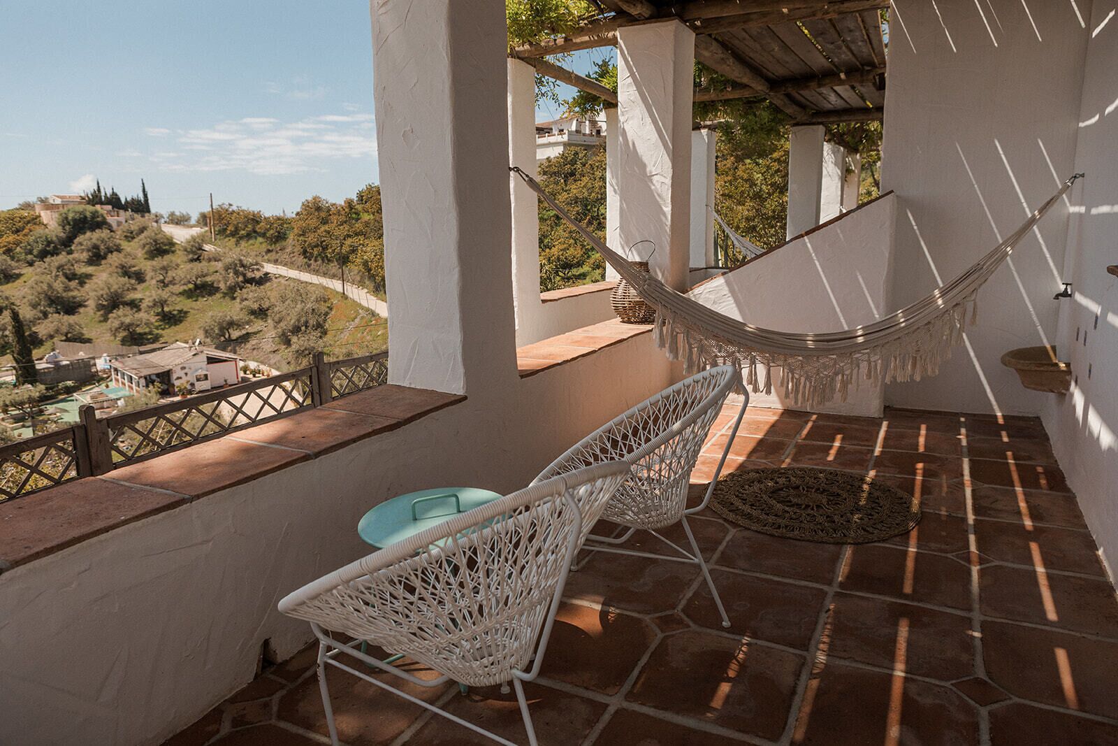 A balcony with a hammock, wicker chairs, and a view of a hilly landscape.
