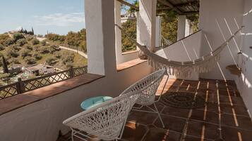 A balcony with a hammock, wicker chairs, and a view of a hilly landscape.