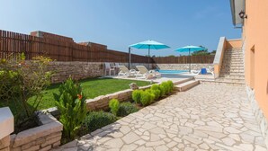 A backyard with a stone patio, a swimming pool, and two blue umbrellas. - Beautiful home in Labin (Labin)
