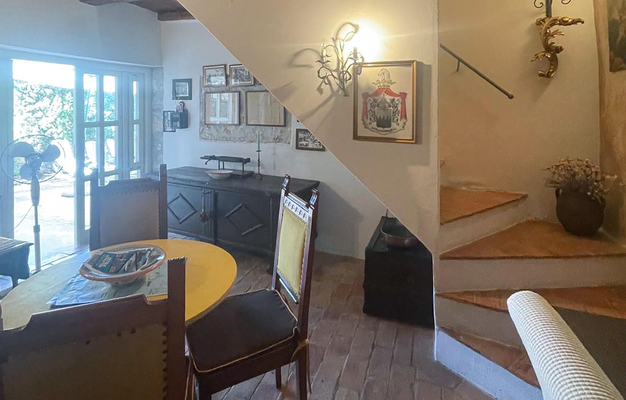 Een eetgedeelte met een ronde tafel en stoelen, een keuken met kasten en een trap die naar boven leidt.
