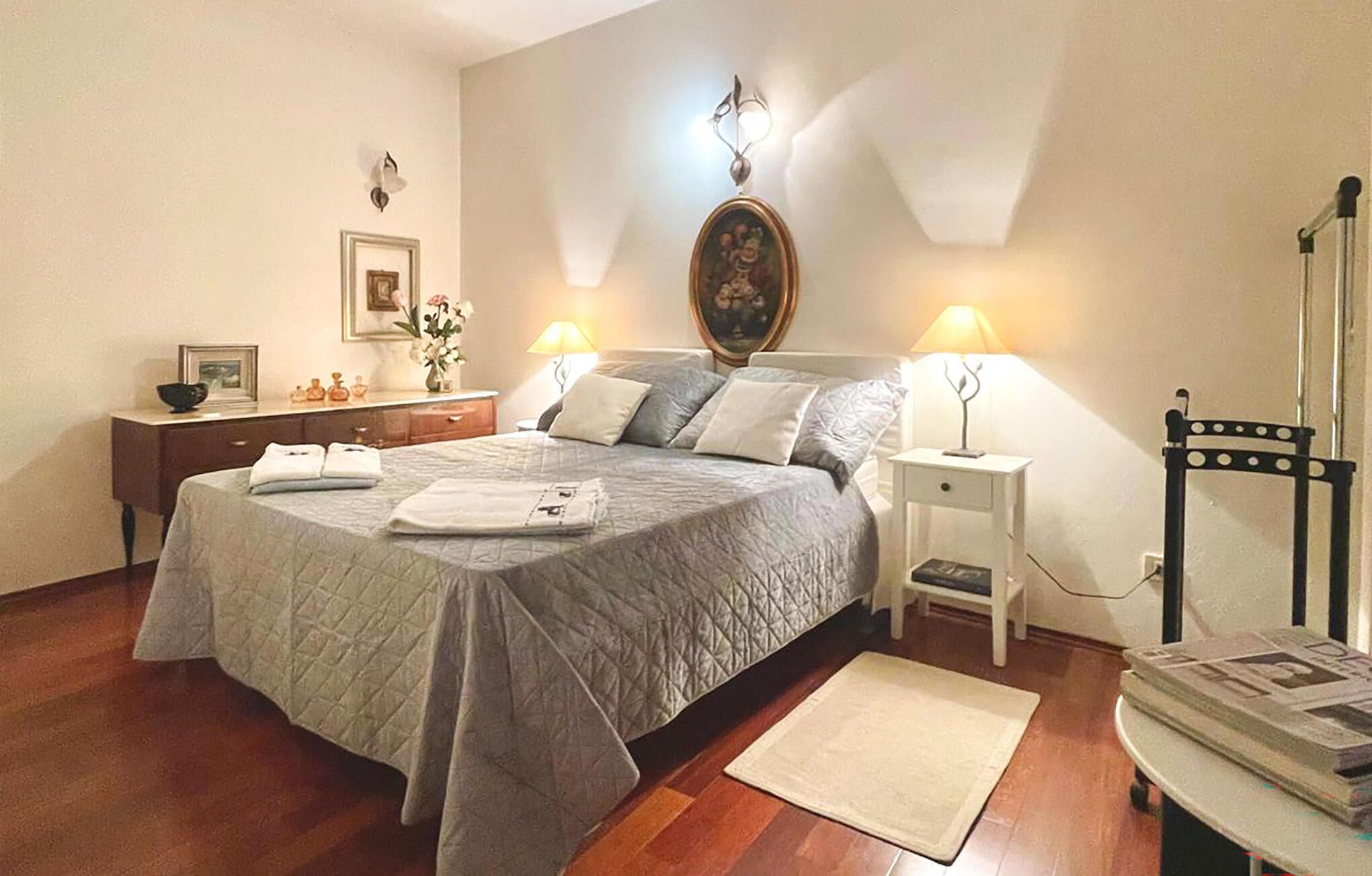 A neatly arranged bedroom with a bed, bedside tables, a nightstand, a chair, and a mirror.