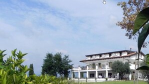 A two-story building with a white facade and a red-tiled roof, surrounded by greenery and trees. - B&B Radici24 (Battipaglia)