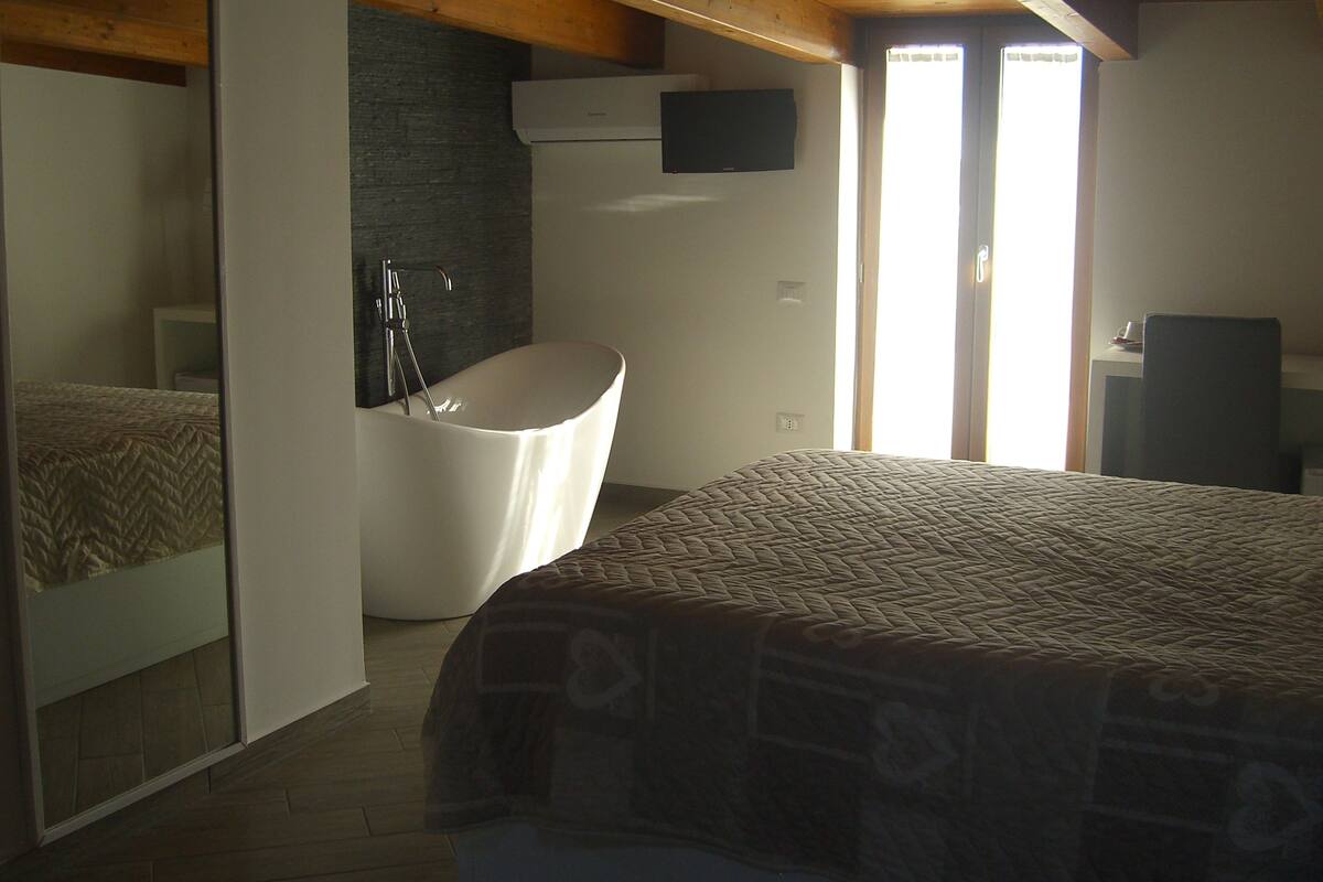 Un dormitorio con una cama grande, una bañera empotrada y un televisor fijado en la pared.