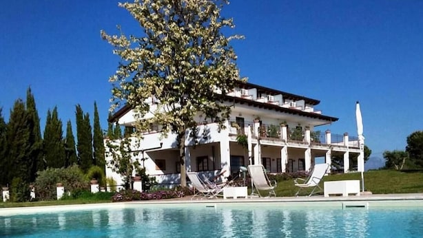 A large building with a swimming pool in front, surrounded by trees and a clear blue sky. - B&B Radici24 (Battipaglia)