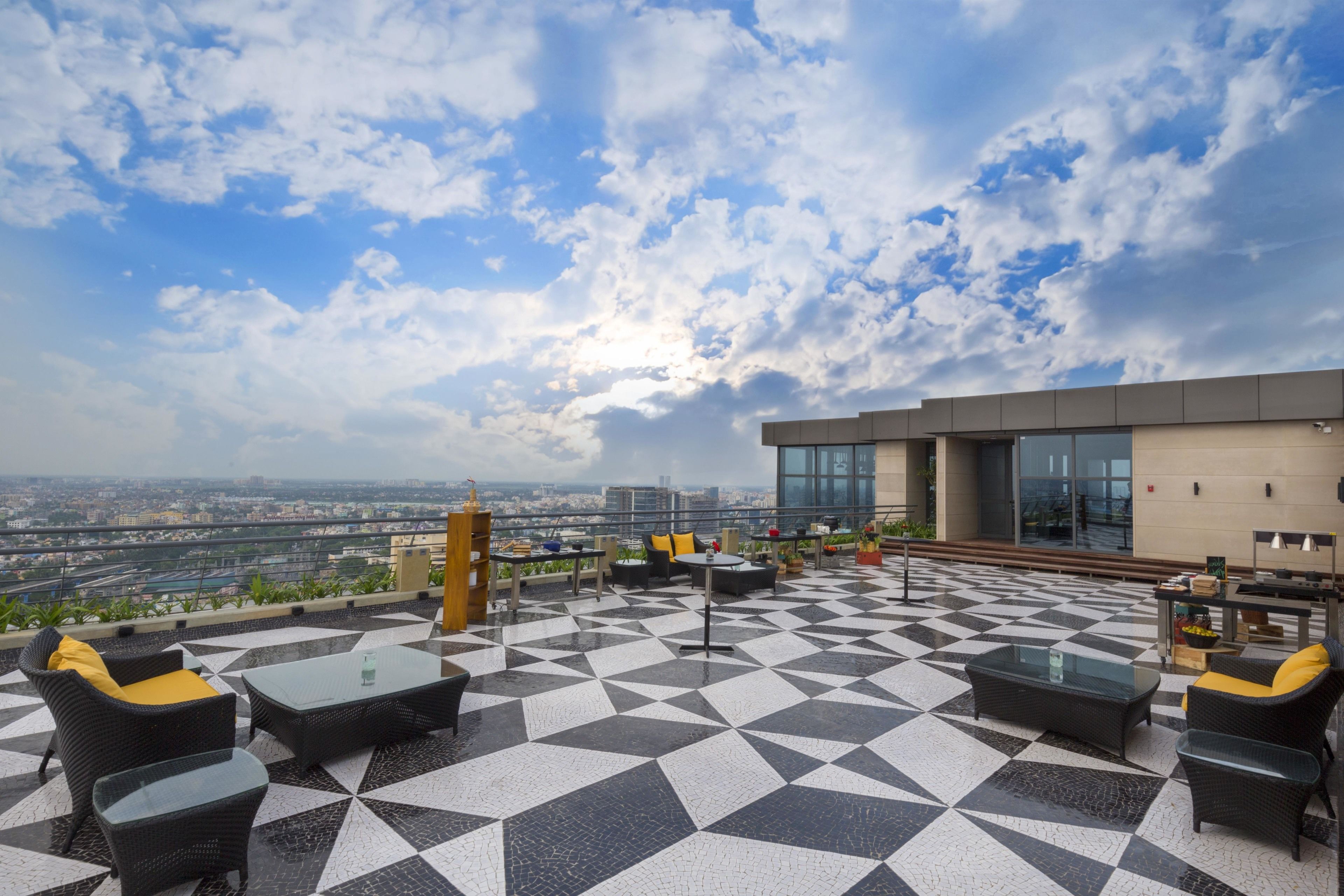 Eine Dachterrasse mit geometrisch gefliestem Boden, Sitzgelegenheiten im Freien und Blick auf die Stadt.