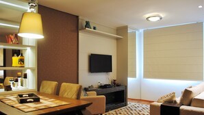 A modern living room with a dining area, a fireplace, and a flat-screen TV mounted on the wall. - Apartamento Flores da Montanha - 052 (Gramado)