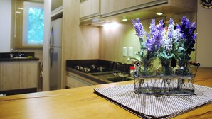 A kitchen with wooden cabinets, a stove, and a vase with flowers on a table. - Apartamento Flores da Montanha - 052 (Gramado)
