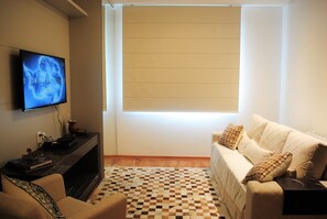 Un salon avec un téléviseur fixé au mur, un canapé, une table basse et un tapis à motifs.