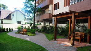 A residential building with a paved garden path, benches, and a pergola. - Apartamento Flores da Montanha - 052 (Gramado)