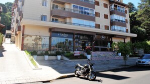 A multi-story building with balconies, a storefront, and a parked motorcycle. - Apartamento Flores da Montanha - 052 (Gramado)