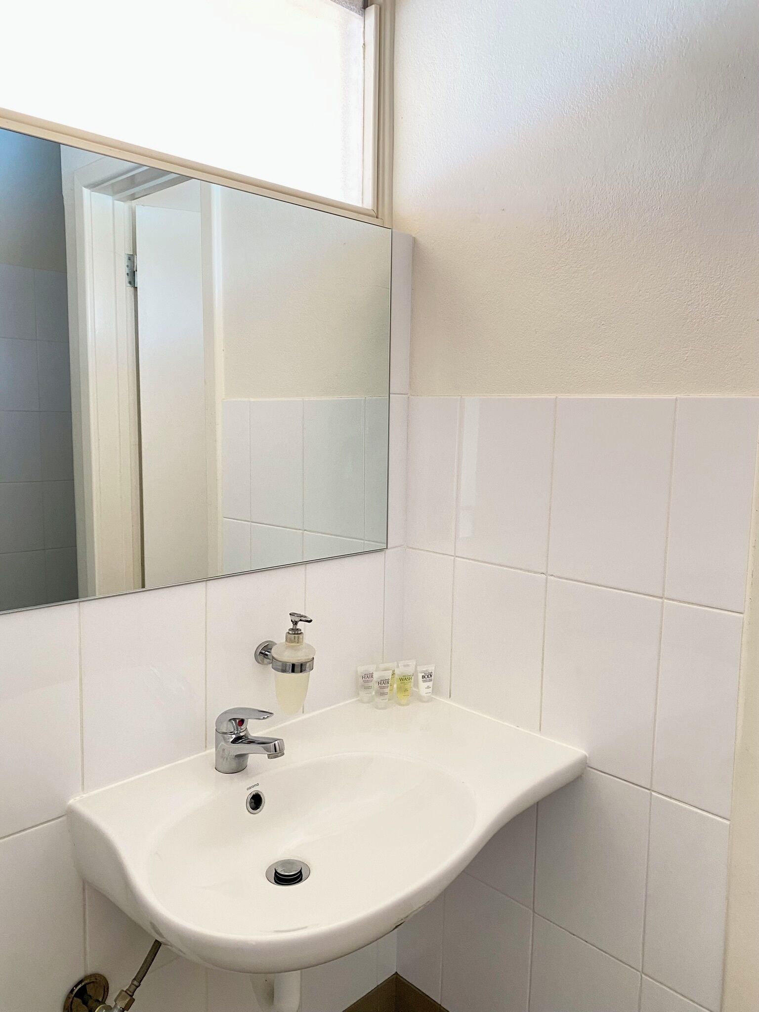 A bathroom with a white sink, a mirror, and toiletries on the counter.