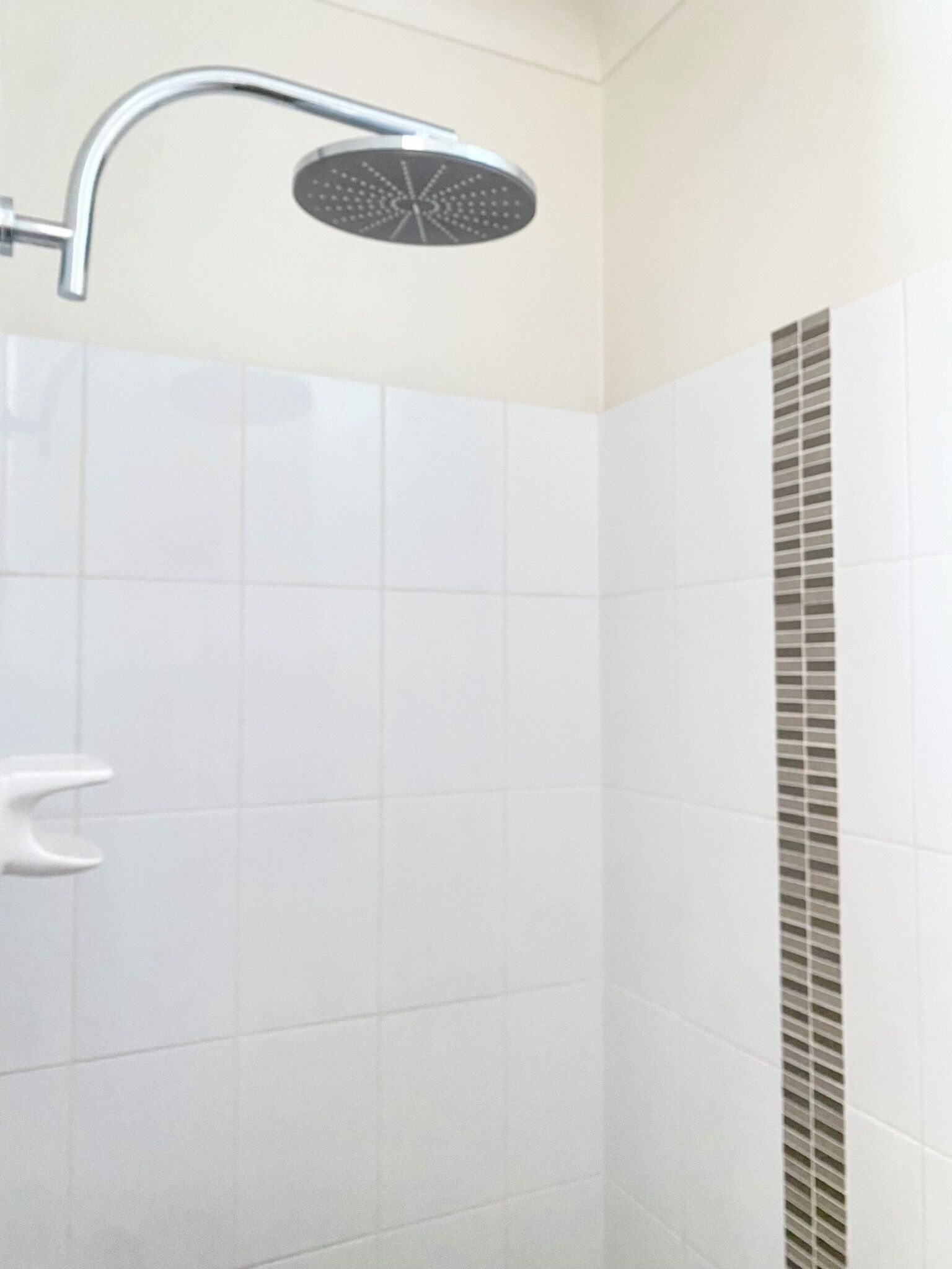 A modern bathroom with white tiles, a shower with a curved handle, and a vent on the wall.