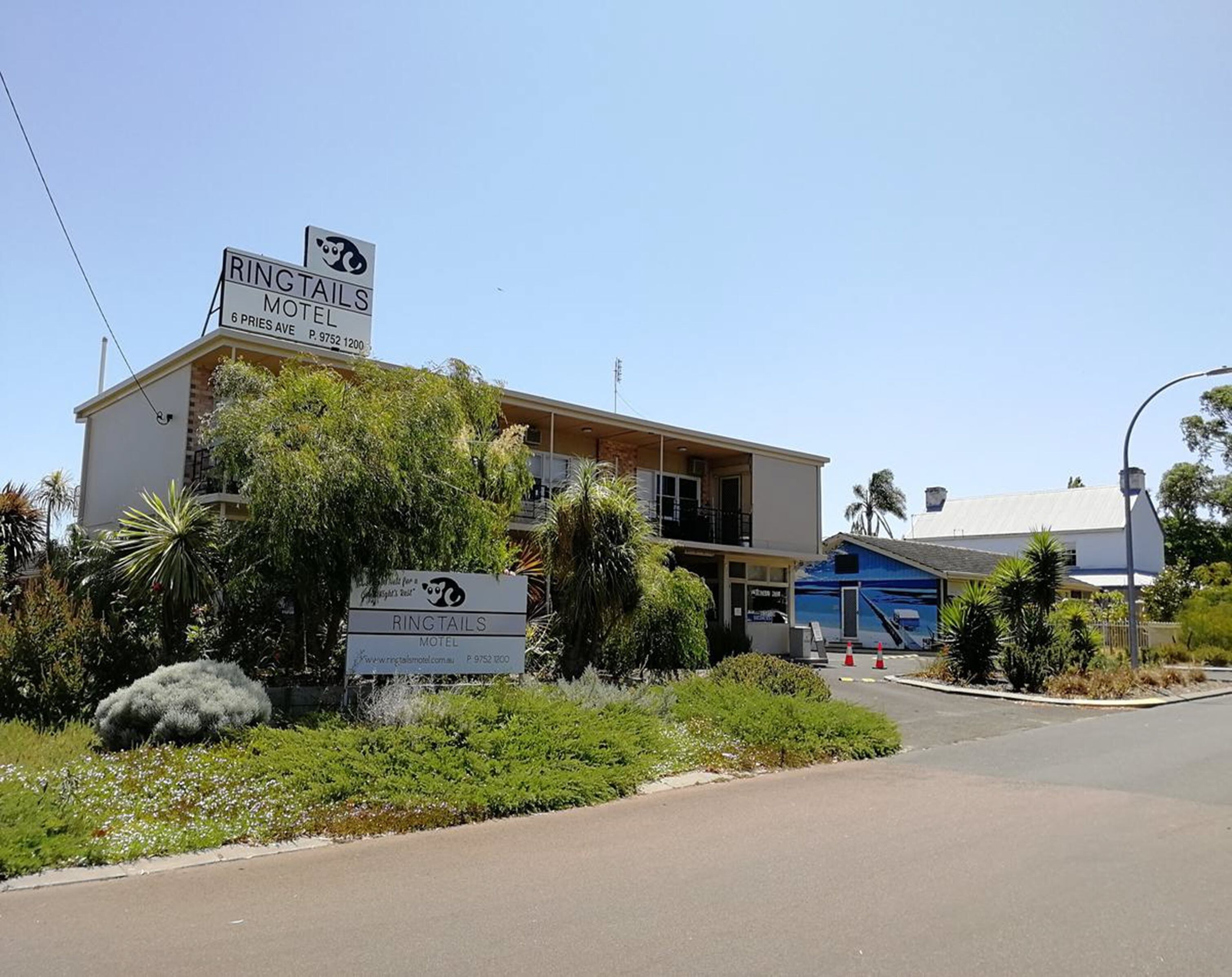 A motel with a signboard, surrounded by greenery and a clear sky.