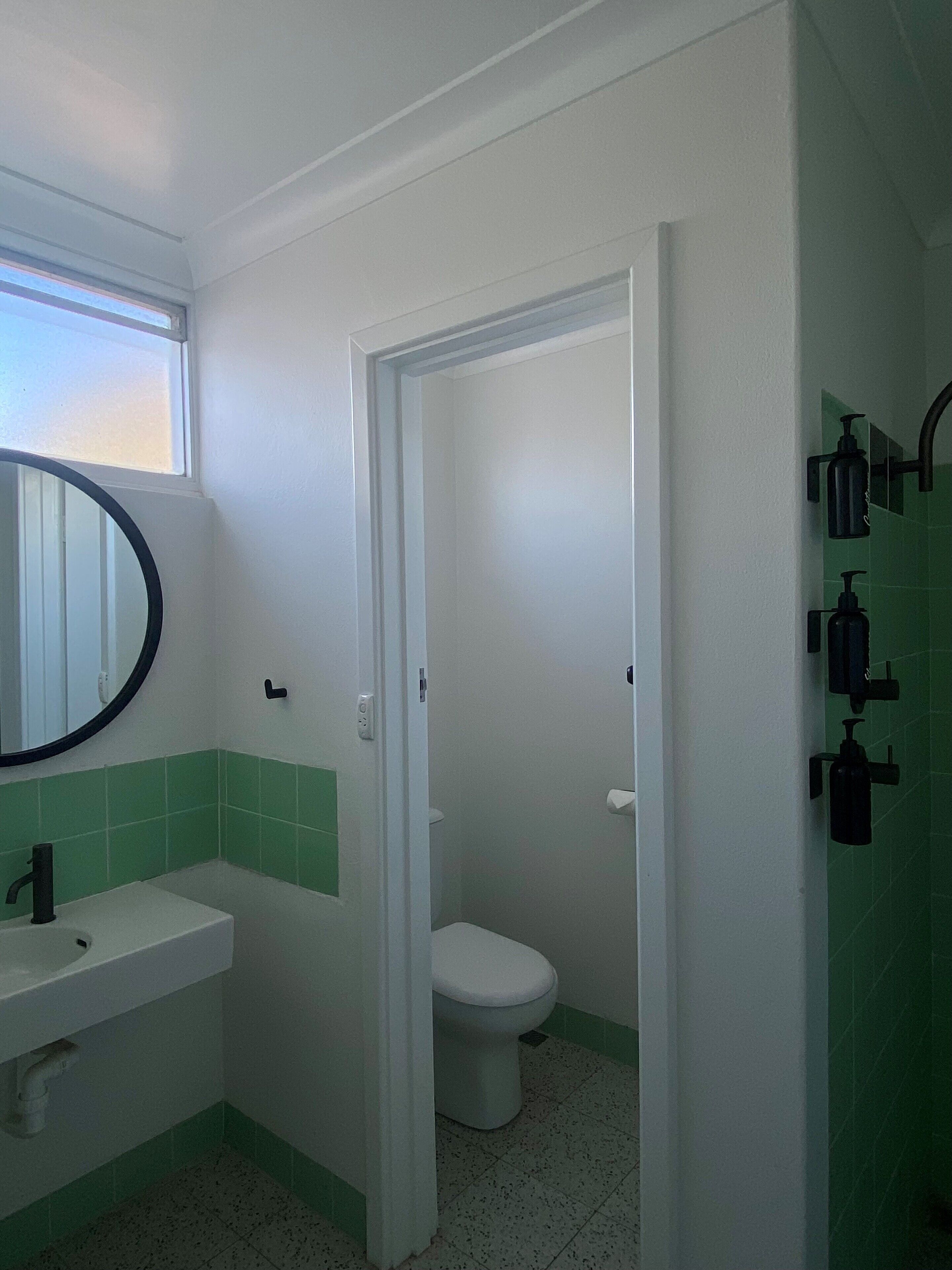 A bathroom with a white sink, green-tiled walls, a white toilet, and a mirror with a black frame.