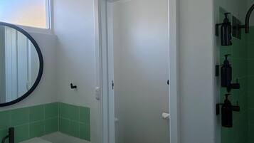 Un baño con un lavamanos blanco, paredes con azulejos verdes, un inodoro blanco y un espejo con marco negro.