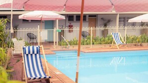 A pool area with striped lounge chairs and umbrellas. - Paradise Motel Busselton (Busselton)