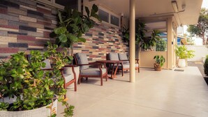 An outdoor seating area with cushioned chairs and tables, a tiled floor, and a wall with a multicolored brick pattern. - Paradise Motel Busselton (Busselton)
