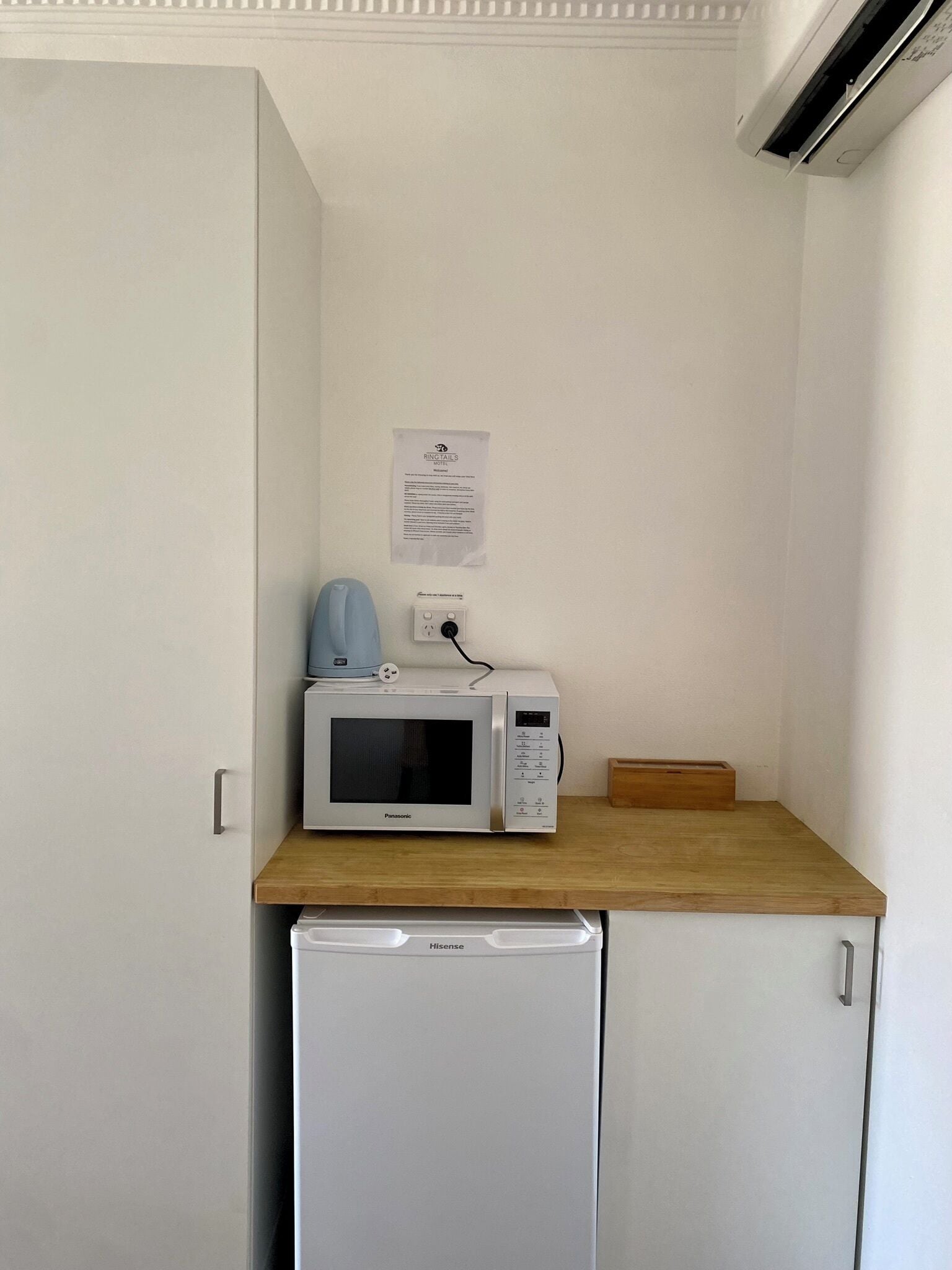 A compact kitchenette with a microwave, a small fridge, and a wooden countertop.