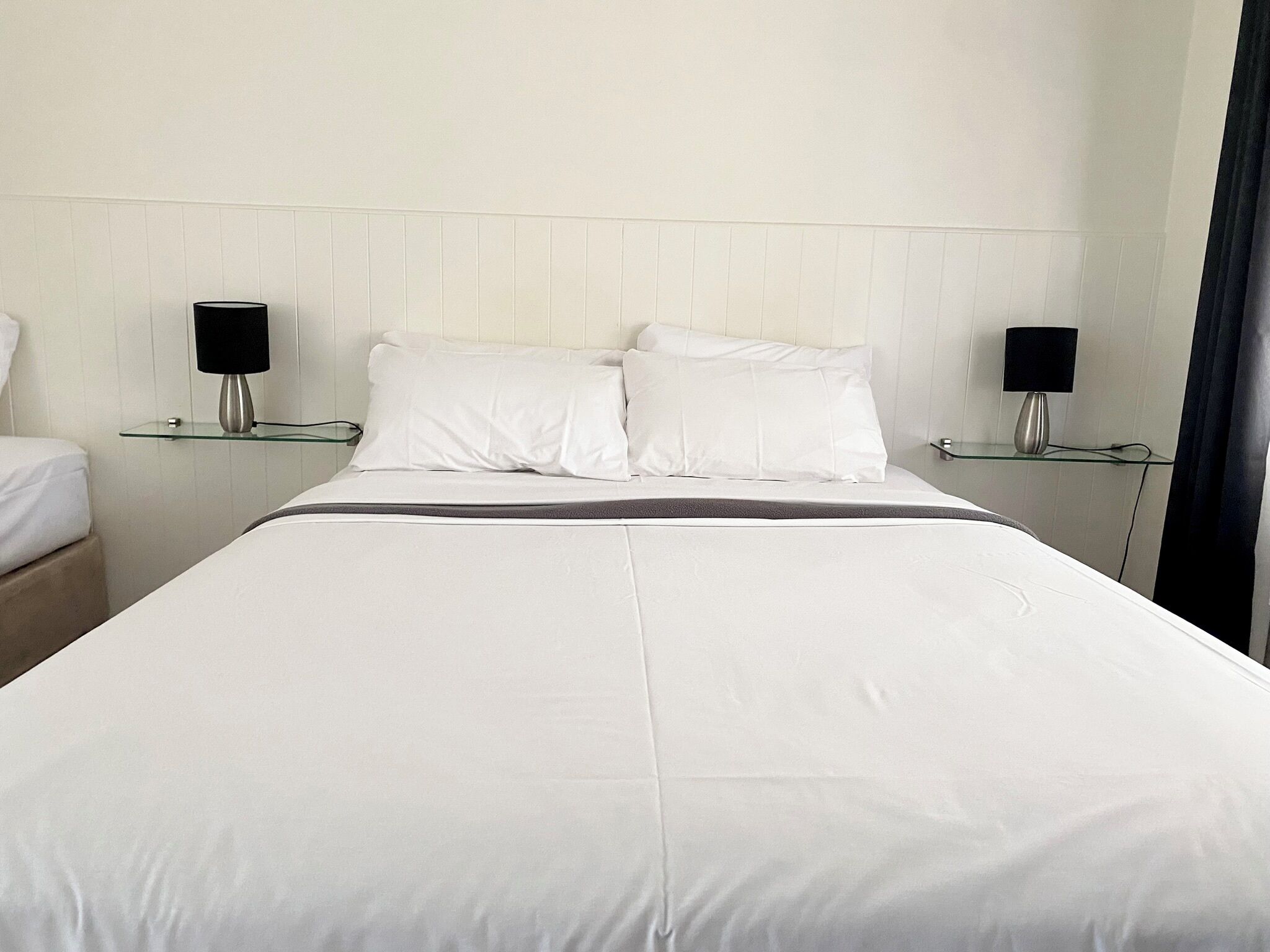 A hotel room with a large bed, two bedside tables, and two lamps.