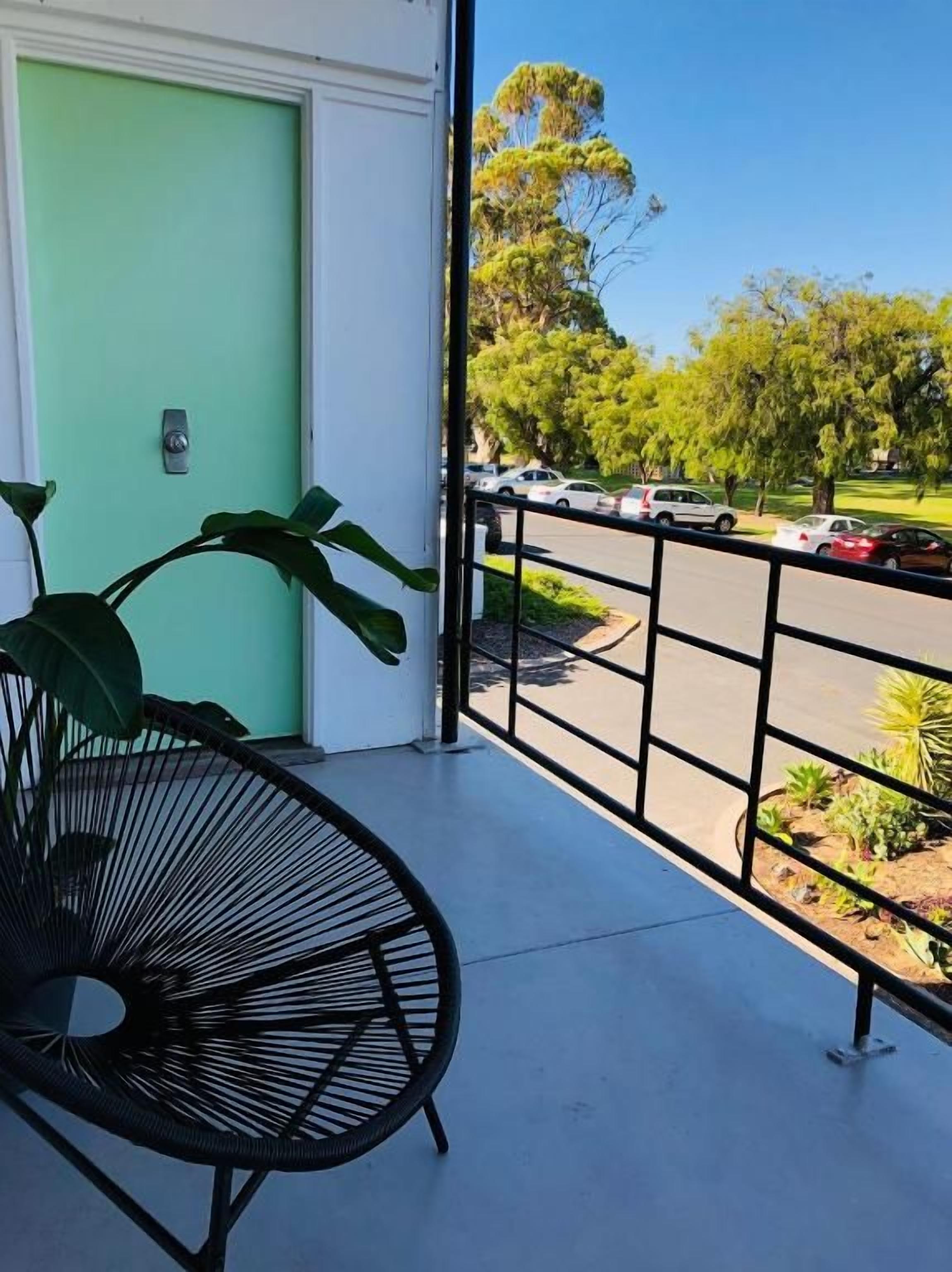 A balcony with a view of a parking area and greenery.
