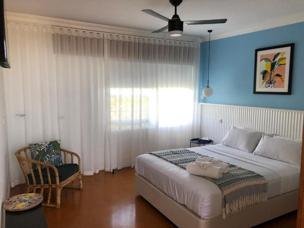 A bedroom with a bed, a chair, a bedside table, and a ceiling fan.
