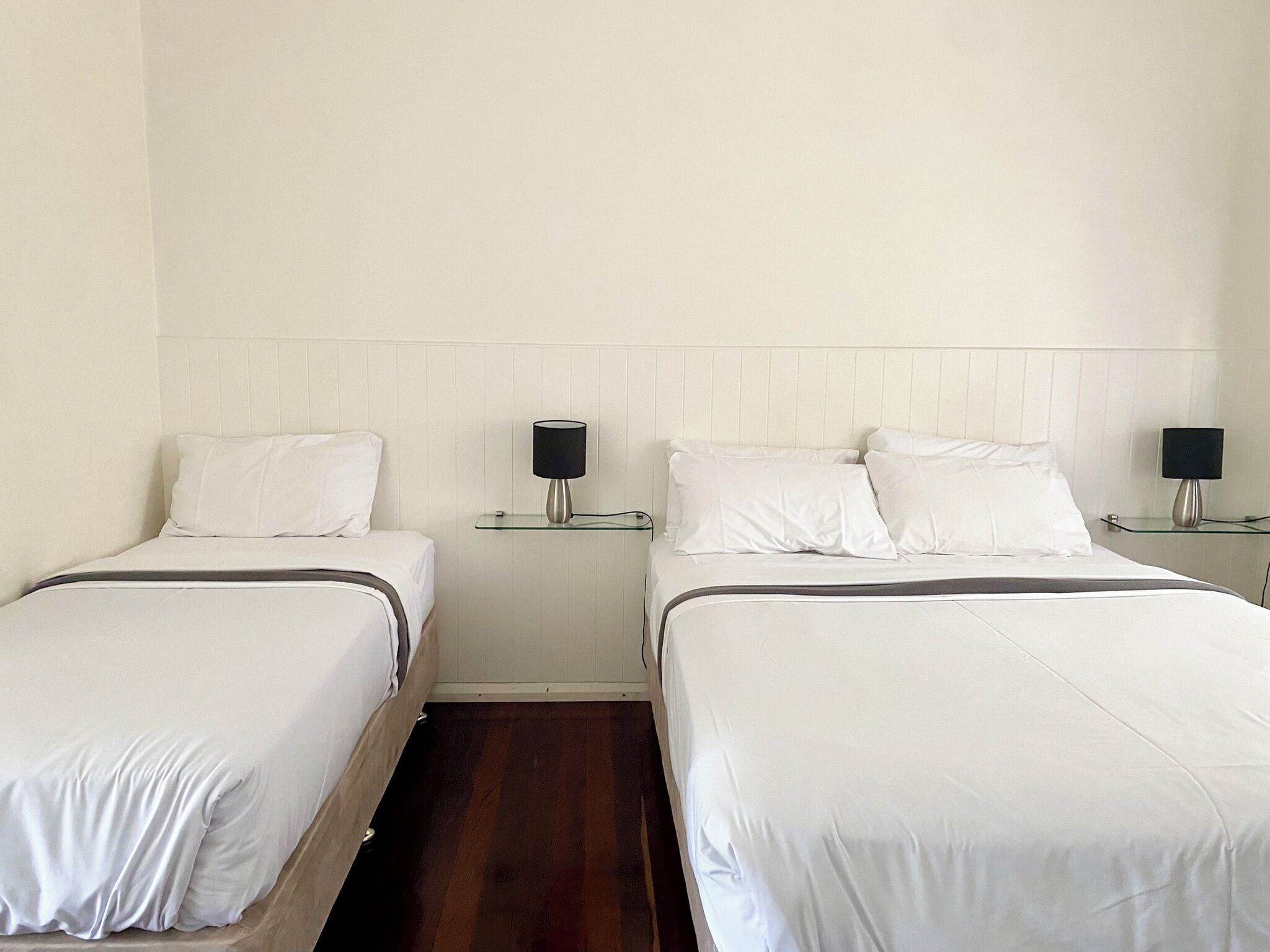 A hotel room with two single beds, each with a bedside table and a lamp.