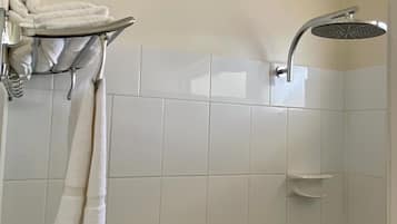 A bathroom with white tiled walls, a shower with a handheld showerhead, and a towel rack with two towels.