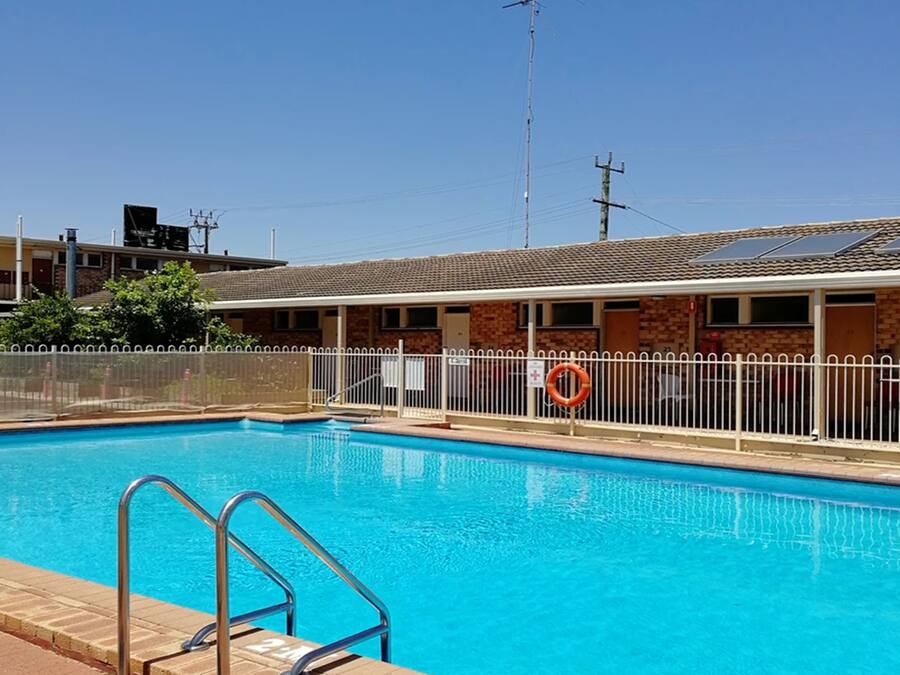 A swimming pool with a metal ladder, a white fence, and a lifebuoy.