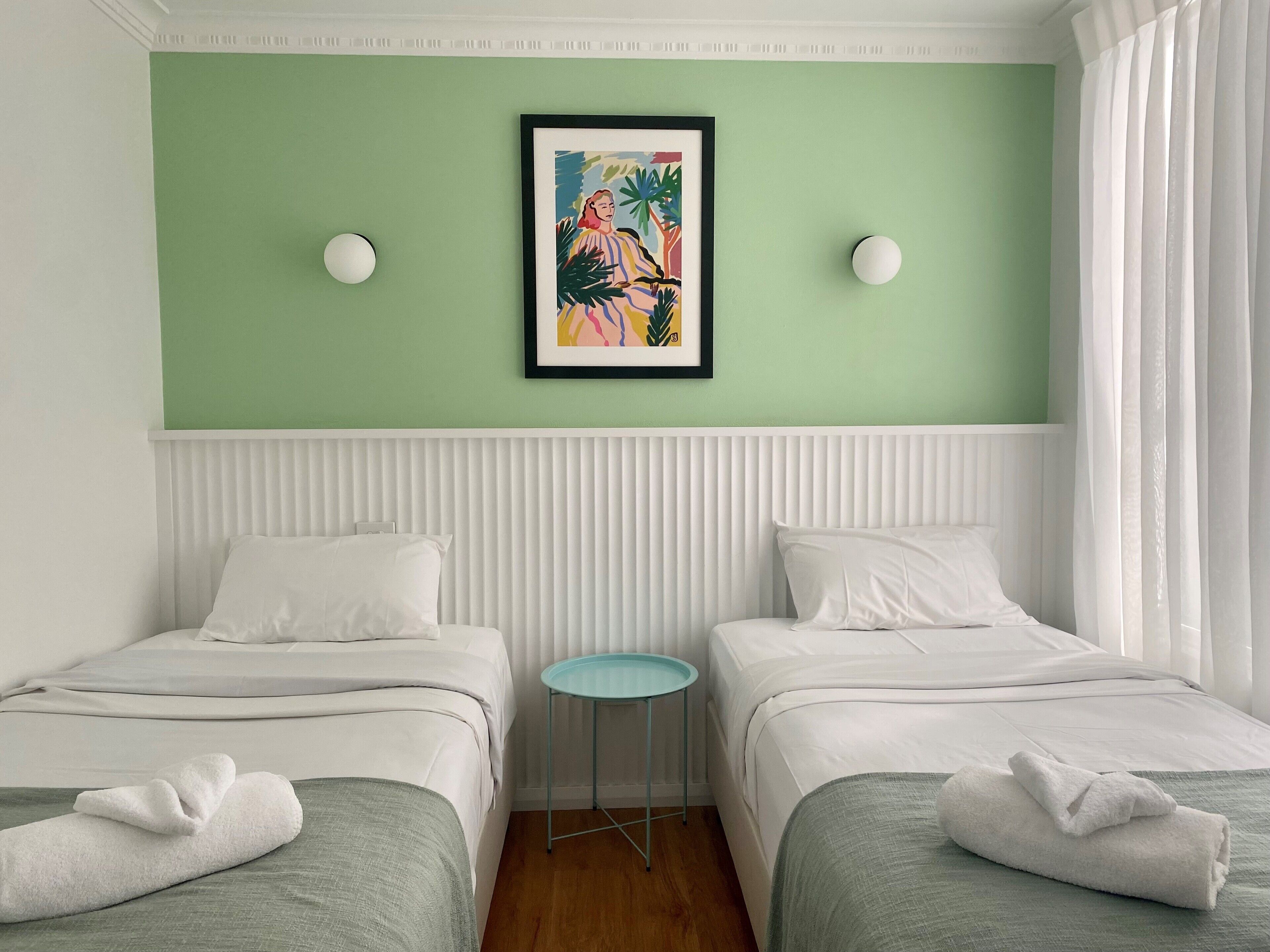 Ein Hotelzimmer mit zwei Betten, einem kleinen runden Tisch und einem gerahmten Gemälde an der Wand.