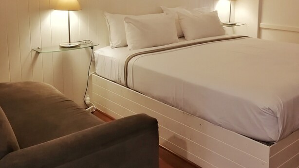 A neatly arranged bedroom with a bed, two bedside lamps, a bedside table, and a chair. - Paradise Motel Busselton (Busselton)