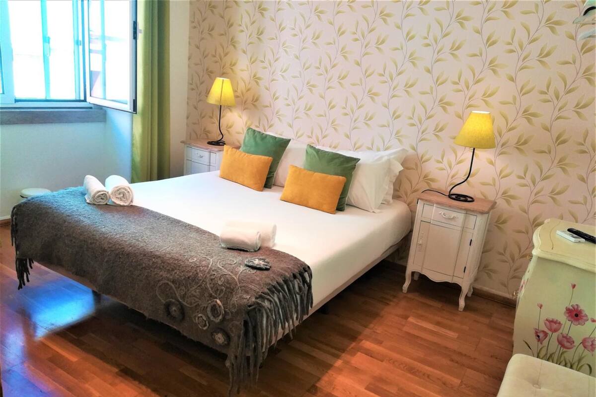 Un lit bien fait, recouvert d’une couverture marron, avec deux lampes de chevet et un papier peint à motifs floraux.