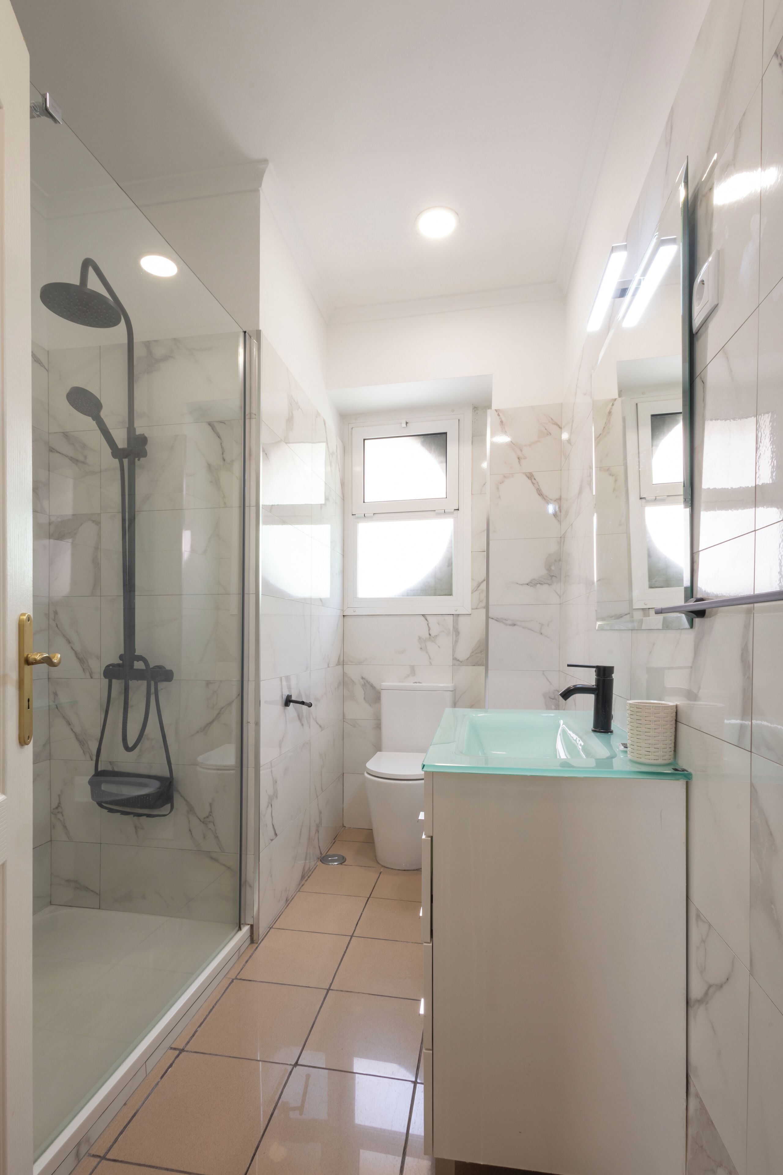 A modern bathroom with a glass shower enclosure, a white marble sink, and a toilet.