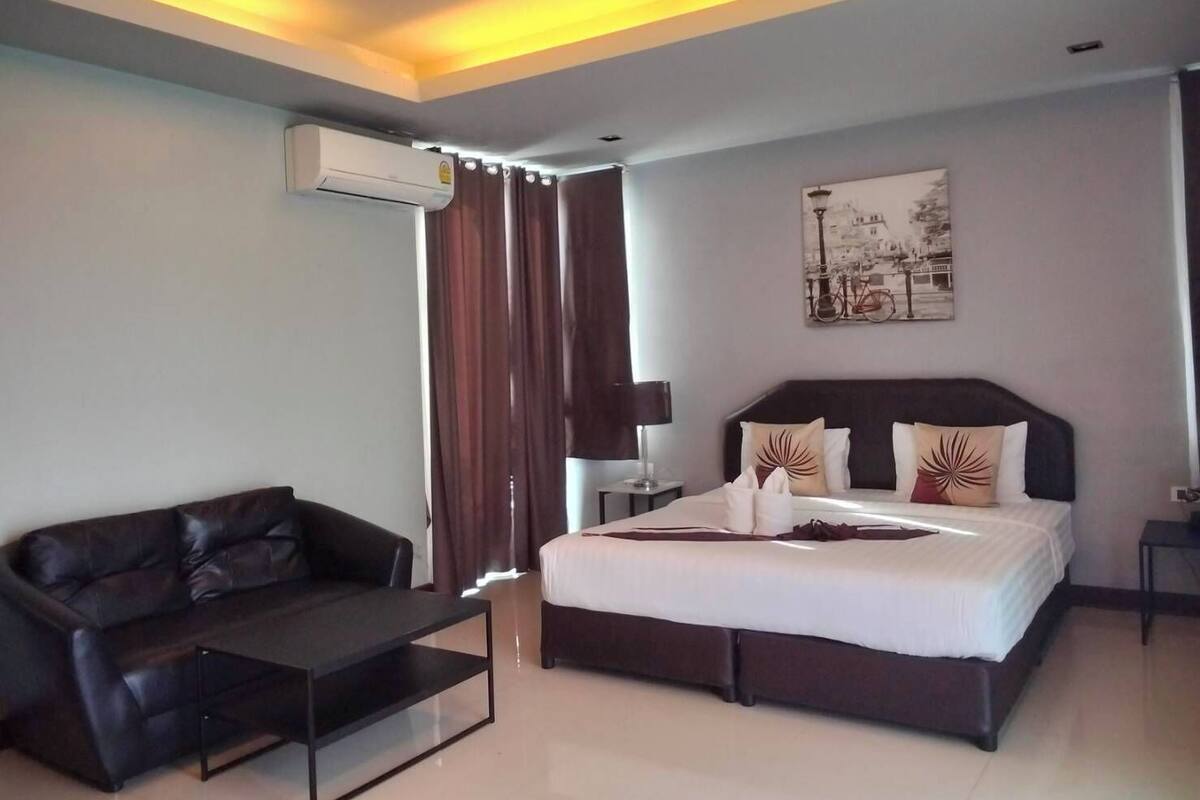 A modern hotel room with a bed, a leather sofa, a coffee table, and a painting on the wall.
