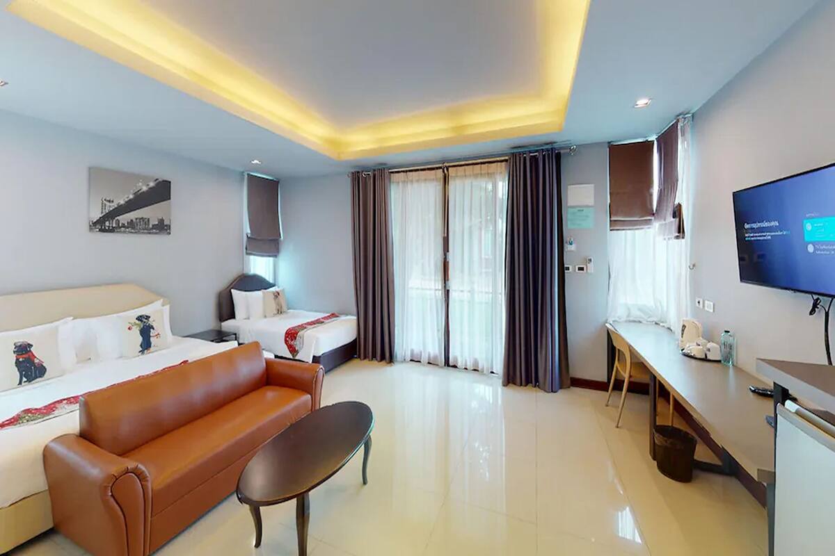 A hotel room with a bed, a sofa, a TV, a desk, and a window with curtains.
