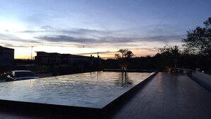 An outdoor swimming pool with a tiled deck, surrounded by buildings and trees, during sunset. - Nutchana Hill Boutique Hotel (Hat Yai)