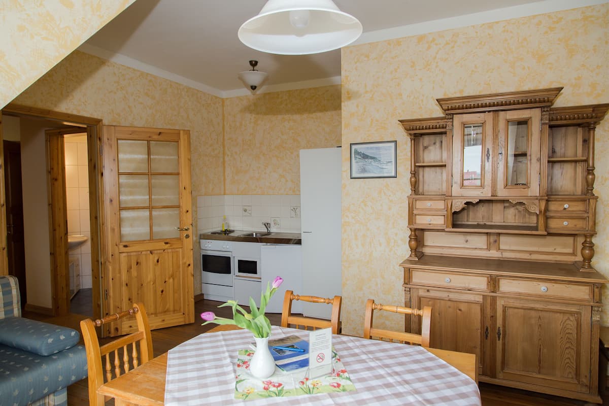 Un coin repas avec une table dressée pour deux personnes, un buffet en bois et une cuisine en arrière-plan.
