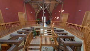 A wooden staircase with a railing leading to a higher floor, surrounded by red walls and wooden beams. - Ostsee-Landhaus (Bastorf)